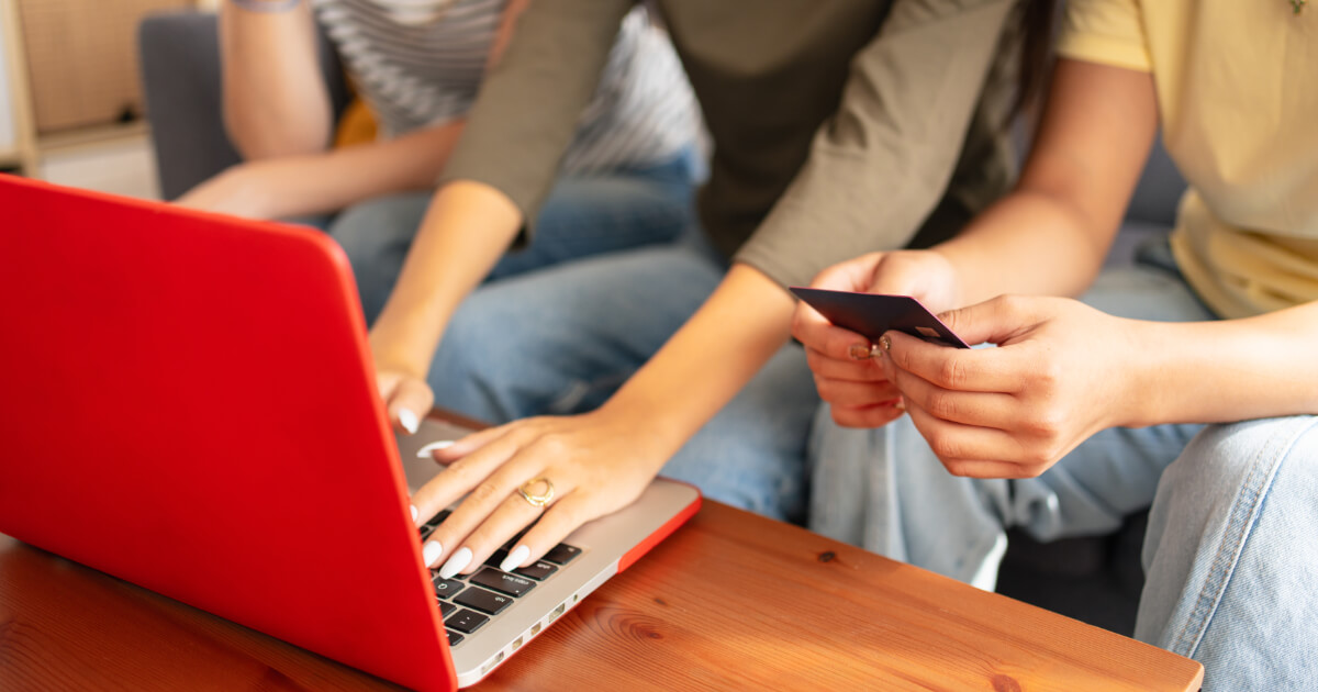 Laptop előtt bankkártyával ülő emberek.
